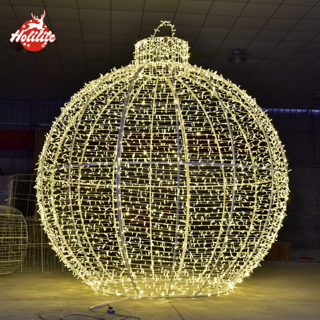 La foto destaca el diseño estructural de la luz con motivo de bola, mostrando su marco de acero galvanizado en caliente y la densa cobertura de la cadena de luces LED. Fabricada para resistir la lluvia, el calor y el frío, esta escultura de iluminación decorativa es adecuada para su instalación a largo plazo en espacios públicos.